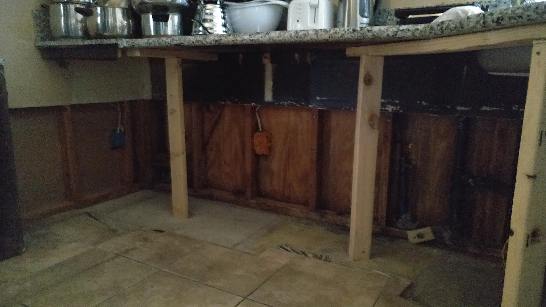 Fontana slab leak kitchen water damage restoration project by PL Builders showing under-cabinet plumbing wall opened after slab leak